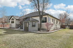 Rear view of house with stucco siding, an outbuilding, a lawn, fence, and brick siding