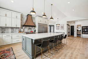 Kitchen featuring lofted ceiling, stainless steel built in fridge, custom range hood, white cabinetry, and a barn door