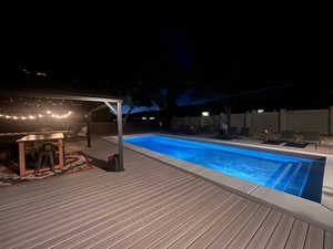 Pool at night featuring a patio area, a fenced in pool, a wooden deck, and fence