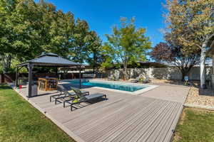 View of swimming pool featuring a fenced in pool, a fenced backyard, a gazebo, a deck, and a lawn