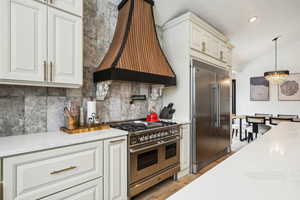 Kitchen featuring custom range hood, tasteful backsplash, white cabinetry, an inviting chandelier, and high end appliances