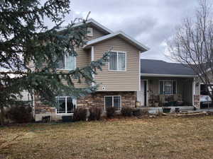 Tri-level home featuring a front lawn, a porch, and stone siding