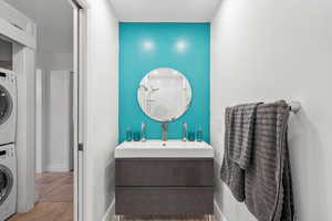 Bathroom featuring tile patterned flooring, baseboards, stacked washing maching and dryer, vanity, and a shower