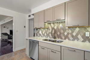 Kitchen featuring visible vents, backsplash, dishwasher, gray cabinets, and a sink