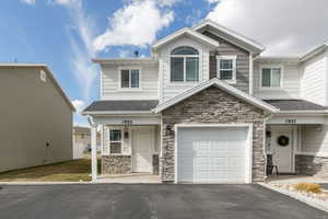 Craftsman-style home featuring aphalt driveway, stone siding, roof with shingles, and an attached garage