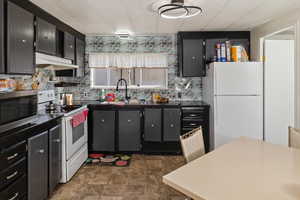 Kitchen with under cabinet range hood, a sink, dark countertops, white appliances, and decorative backsplash