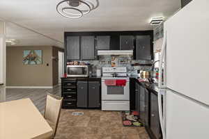 Kitchen featuring visible vents, under cabinet range hood, backsplash, dark countertops, and white appliances