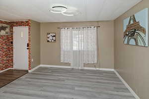 Spare room with brick wall, baseboards, and wood finished floors