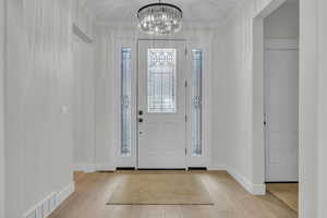 Entrance foyer featuring visible vents, a notable chandelier, wood finished floors, and ornamental molding