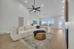 Living area featuring light wood-type flooring, visible vents, high vaulted ceiling, ceiling fan with notable chandelier, and baseboards