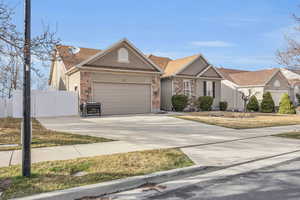 View of front of home with stucco siding, stone siding, fence, concrete driveway, and a garage