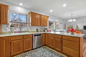 Kitchen featuring a sink, stainless steel dishwasher, a peninsula, light countertops, and a healthy amount of sunlight