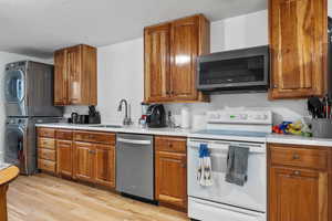 Kitchen featuring white range with electric cooktop, a sink, stainless steel dishwasher, stacked washer / dryer, and brown cabinets