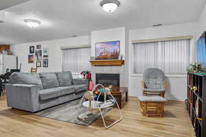 Living room featuring a textured ceiling, baseboards, light wood-type flooring, and a tile fireplace