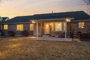 Rear view of house featuring a yard, a patio, brick siding, and roof with shingles