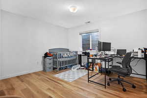 Office area featuring wood finished floors, visible vents, and baseboards
