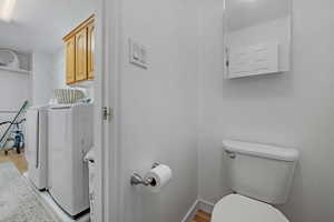 Bathroom with baseboards, toilet, wood finished floors, a textured ceiling, and separate washer and dryer