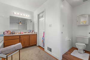 Full bathroom with vanity, wood finished floors, visible vents, baseboards, and toilet