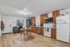 Kitchen featuring stainless steel appliances, light wood-style floors, brown cabinetry, light countertops, and stacked washer / dryer