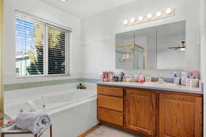 Bathroom featuring ceiling fan, a garden tub, a stall shower, and vanity