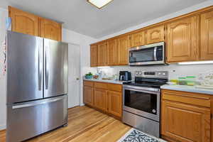 Kitchen featuring brown cabinetry, appliances with stainless steel finishes, light wood-type flooring, and light countertops