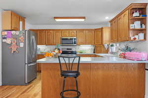 Kitchen with a sink, appliances with stainless steel finishes, a peninsula, light wood finished floors, and light countertops