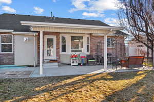 Rear view of property featuring a patio, fence, a yard, a shingled roof, and brick siding