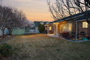 Yard at dusk with a trampoline, fence, a storage shed, an outdoor structure, and a patio area