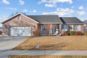 Ranch-style home featuring brick siding, a shingled roof, a front yard, driveway, and an attached garage