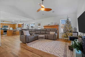 Living room featuring lofted ceiling, ceiling fan with notable chandelier, and light wood-type flooring