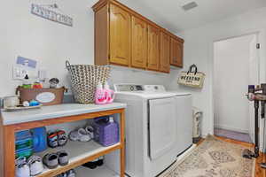 Washroom featuring visible vents, light wood-style flooring, washer and clothes dryer, cabinet space, and baseboards