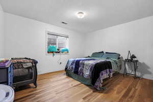 Bedroom with visible vents, baseboards, a textured ceiling, and wood finished floors