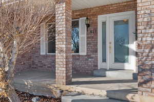 Doorway to property featuring brick siding and covered porch