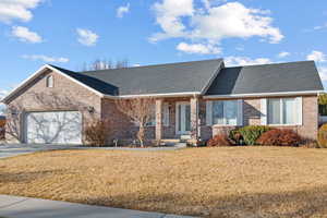 Ranch-style house featuring brick siding, a shingled roof, a front lawn, a garage, and driveway