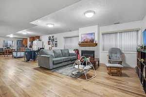 Living area featuring a tile fireplace, light wood finished floors, and a textured ceiling