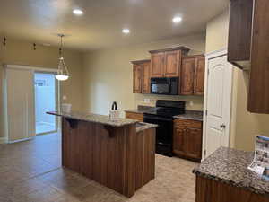 Kitchen featuring hanging light fixtures, a breakfast bar area, dark stone counters, black appliances, and a kitchen island