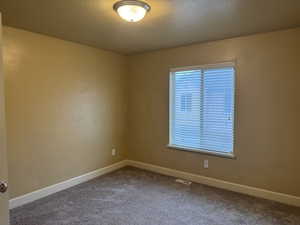 Carpeted spare room featuring a textured ceiling, baseboards, and visible vents
