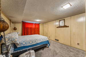 Carpeted bedroom with wooden walls, visible vents, and a textured ceiling