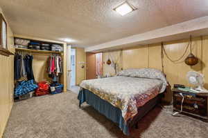 Carpeted bedroom featuring a closet, wooden walls, and a textured ceiling