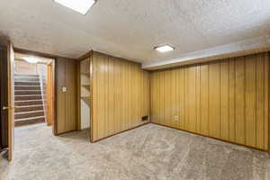 Finished basement featuring visible vents, light carpet, a textured ceiling, stairway, and wood walls