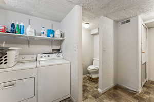 Laundry room with washing machine and clothes dryer, visible vents, baseboards, wood finished floors, and a textured ceiling