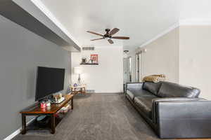 Carpeted living area with visible vents, baseboards, ceiling fan, and ornamental molding