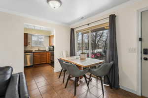 Dining room with dark tile patterned floors, visible vents, crown molding, and baseboards