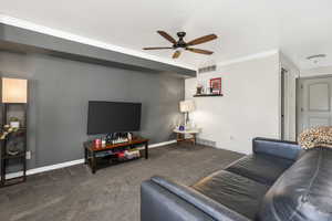 Carpeted living area with visible vents, baseboards, a ceiling fan, and crown molding