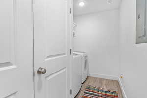 Washroom featuring baseboards, laundry area, light wood-style flooring, electric panel, and washer and dryer