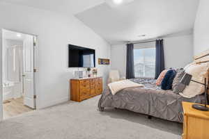 Bedroom with lofted ceiling, light colored carpet, visible vents, and baseboards
