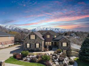 View of front facade with stone siding, a mountain view, driveway, and fence