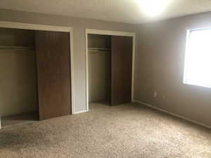 Unfurnished bedroom with baseboards, multiple closets, a textured ceiling, and carpet floors