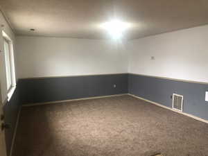 Spare room featuring baseboards, visible vents, a textured ceiling, and carpet