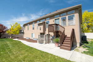 Rear view of house featuring fence, central air condition unit, stucco siding, and a lawn